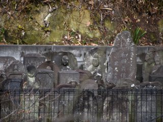 Solemn faces of dark stone jizo statues and tomb stones