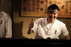 Having some fun cooking in the back, signs behind him show types of yakitori