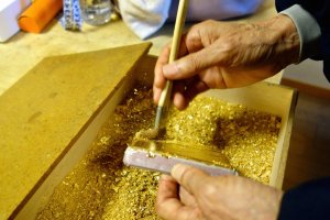 The craftsmaster adheres the gold leaf to the box lid by brushing with gold dust