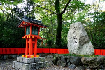 <p>A red wooden lantern and an inscribed rock stand at the entrance to Shimogamo Shrine</p>