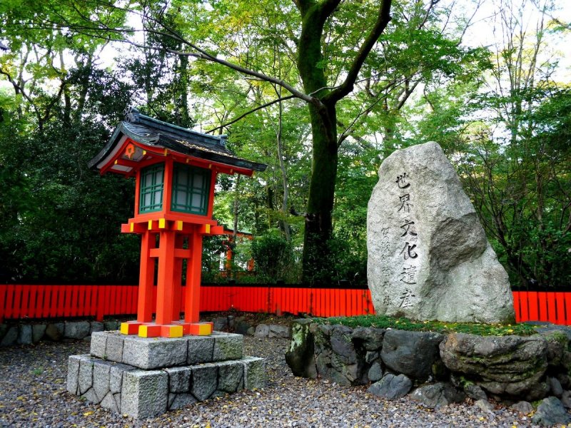 <p>A red wooden lantern and an inscribed rock stand at the entrance to Shimogamo Shrine</p>