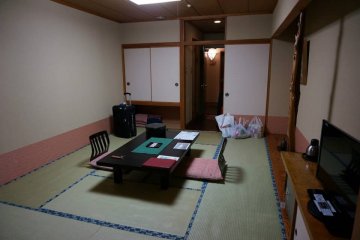 <p>ภายในห้องพักก่อนที่พนักงานจะมาปูที่นอนให้ จะมีโต๊ะและเก้าอี้นั่งแบบญี่ปุ่นตั้งอยู่กลางห้องให้นั่งพักผ่อน</p>