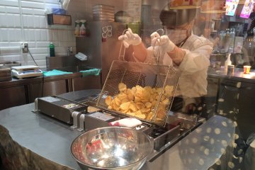 Peeking through the glass window, attentively watching them prepare freshly fried potato chips. Get them while they&#39;re hot!