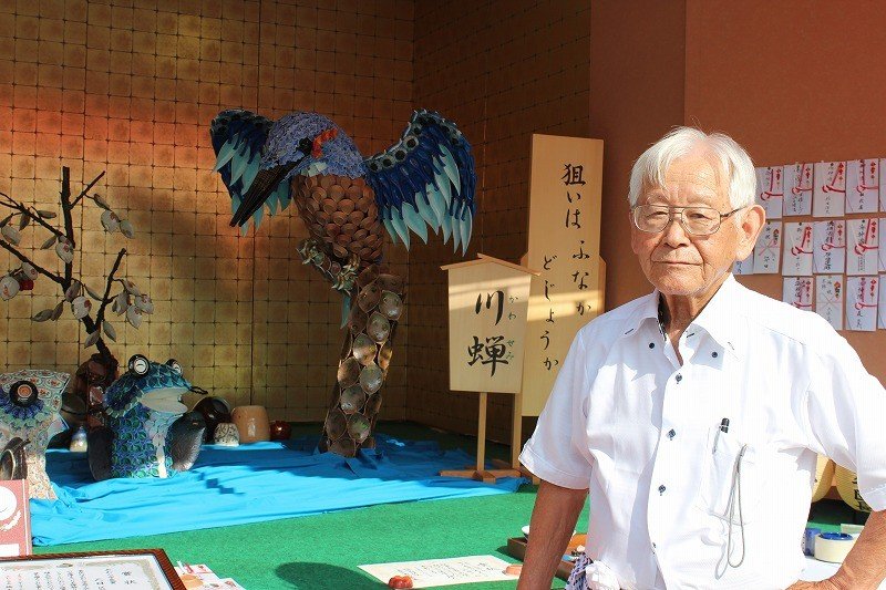 金津町六日区本陣の飾り物を仕切る稲田信夫さん。陶器の小皿を使い、カワセミと魚の鳥獣戯画のような場面を描いている