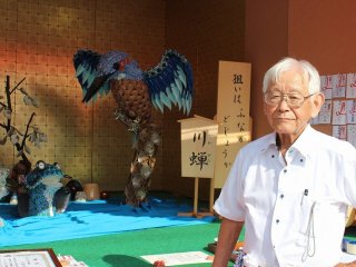金津町六日区本陣の飾り物を仕切る稲田信夫さん。陶器の小皿を使い、カワセミと魚の鳥獣戯画のような場面を描いている