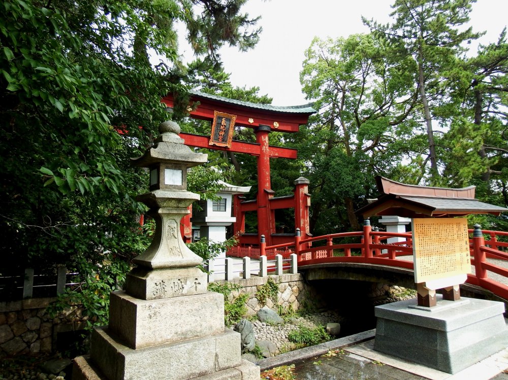 気比神宮正面入り口。緑に囲まれた赤い鳥居と朱塗りの小さな橋、石灯籠が美しい