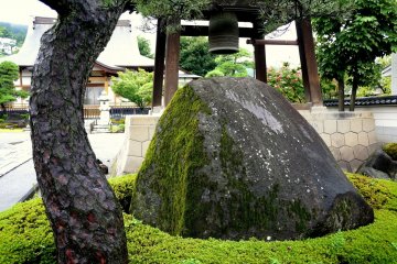 <p>A large mossy rock stands beside the bell tower</p>