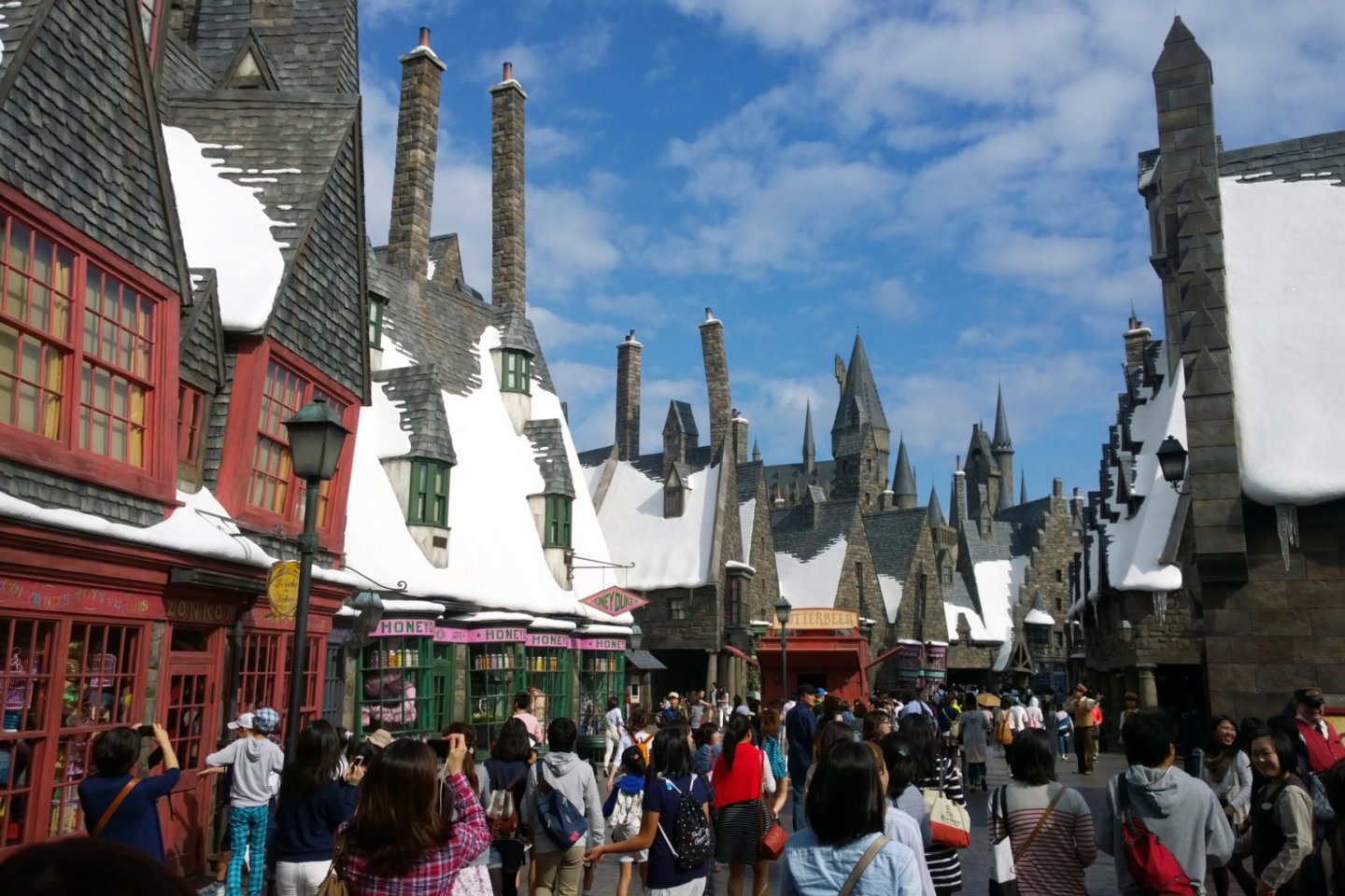 The Wizarding World of Harry Potter : ผู้คนมากมายกำลังสนุกสนานอยู่ในบริเวณหมู่บ้าน HOGSMEADE VILLAGE ที่ถอดแบบจินตนาการเมืองแห่งเวทมนตร์มาจากบทประพันธ์และภาพยนตร์ให้เราสัมผัสได้จริง หมู่บ้านแห่งนี้เป็นด่านแรกที่จะต้อนรับเราสู่ The Wizarding World of Harry Potter อาคารต่างๆ นั้นดูผิดส่วนแปลกตาสวยงามอย่างน่าอัศจรรย์ ตลอดถนนกลางหมู่บ้านนั้นมีร้านรวงที่น่าสนใจมากมายที่ราวรุดมาจากมหากาพย์ชื่อดังแห่งยุคนี้เลยทีเดียว อาทิ ร้านขนมหวาน HONEYDUKES, ร้านไปรษณีย์นกฮูก OWL POST & OWLERY, ร้านไม้กายสิทธิ์ OLLIVANDERS เป็นต้น