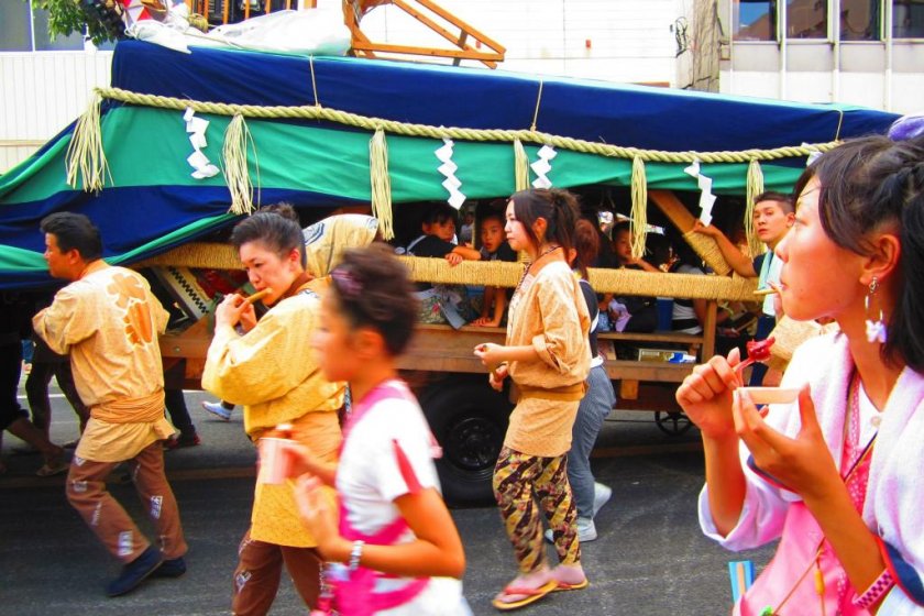 A lion-dance cart flanked by locals dressed in parade gear playing and singing accompanying music