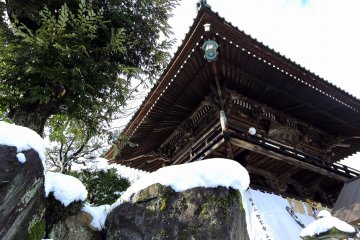 <p>Main gate with snow-capped rocks beside it at the entrance to Shougenji Temple in Fukui</p>
