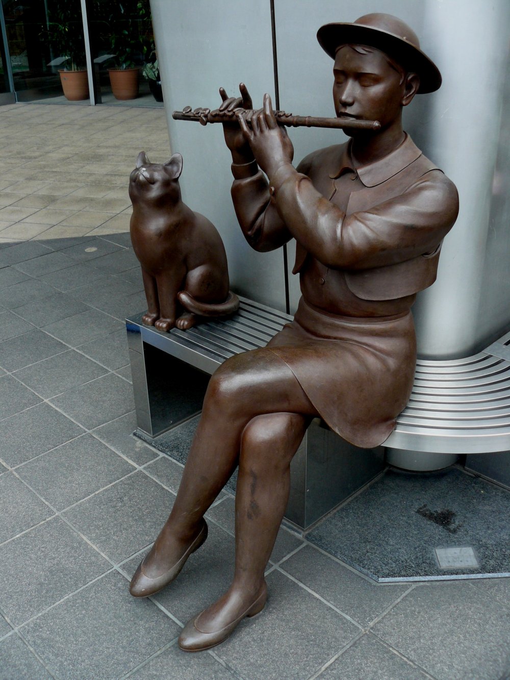 Бронзовая девушка играет на флейте, сидя на лавочке