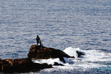 <p>The view from Kikaigaura Observation Deck with a fisherman on a rock in a calm sea</p>