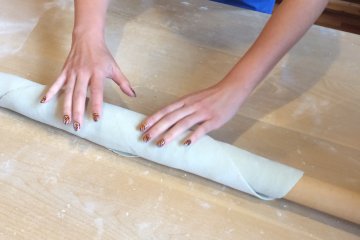 <p>Carefully rolling the dough around the pin.</p>