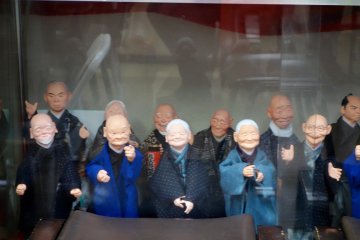 A merry bunch of elderly-faced puppets sit on display in a glass cabinet