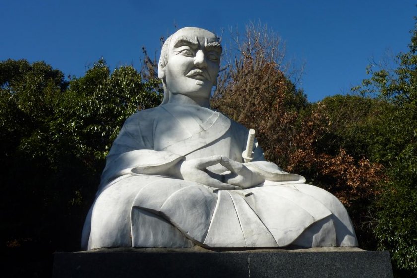 A large statue of Miyamoto Musashi looms over the parking lot