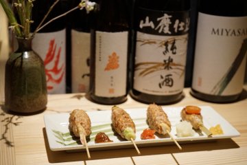 Grilled chicken meatball skewers alongside Japanese sake bottles