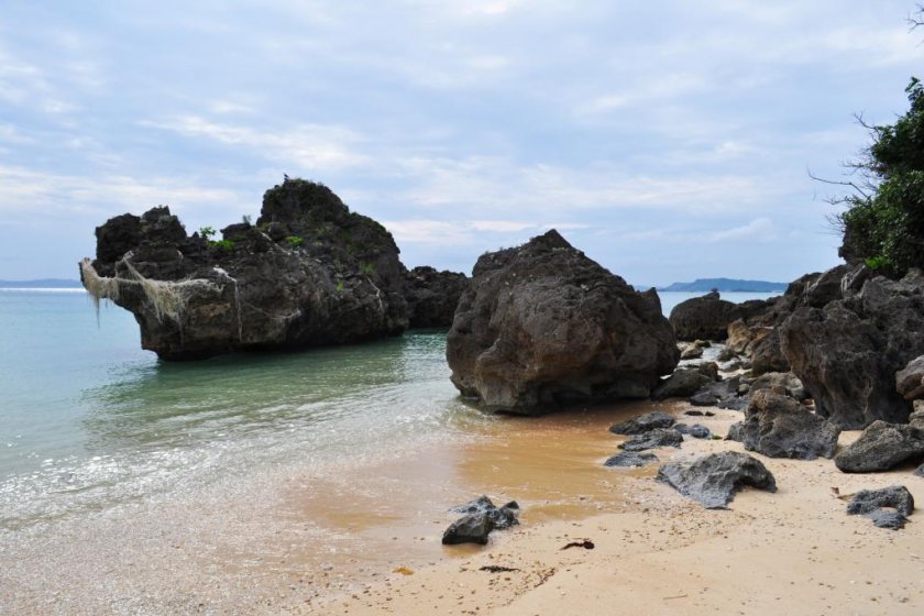 A tropical paradise complete with soft sand, clear water and a rock to jump off into the water.