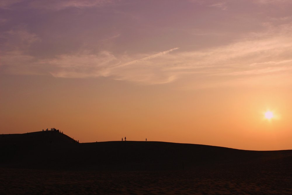 Beaucoup de gens se rassemblent sur la plus grande des dunes pour regarder le soleil descendre sous l&#39;horizon