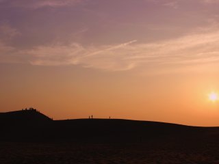 Beaucoup de gens se rassemblent sur la plus grande des dunes pour regarder le soleil descendre sous l&#39;horizon