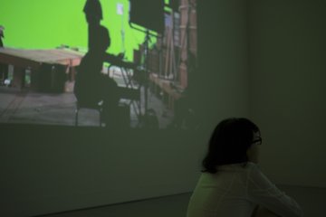 A woman watches the main film while the making of is projected just to her left