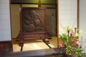 The first door on the left is not for guests, although it used to be. The space is decorated with a wooden carved screen on a tatami mat behind a shoji (paper sliding) door. The figure is called “Hotei” which is one of seven deities of good fortune.